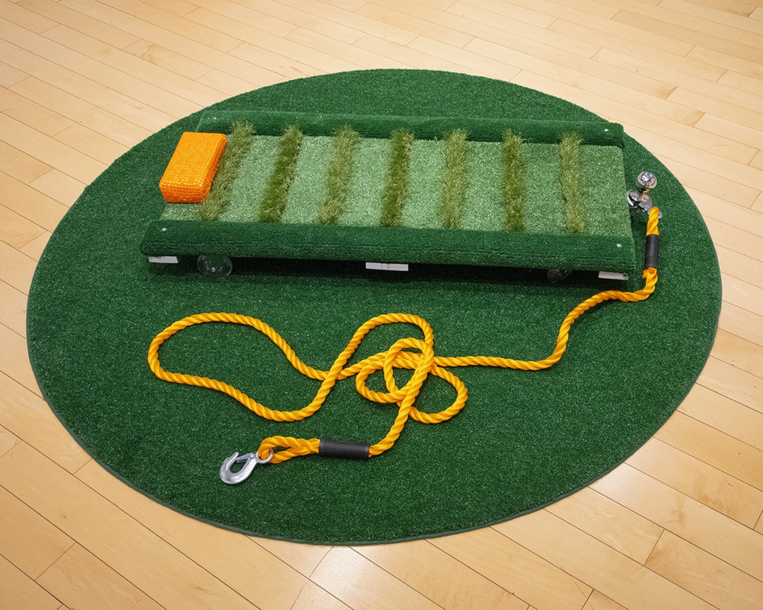 Rachel Merrill, Untitled (Creeper), 2019, Artificial turf, wood, caster wheels, trailer hitch, and tow rope, 56x56x4 in., Collection of the artist